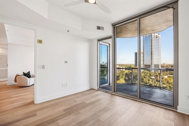 empty room with ceiling fan, light hardwood / wood-style floors, and expansive windows