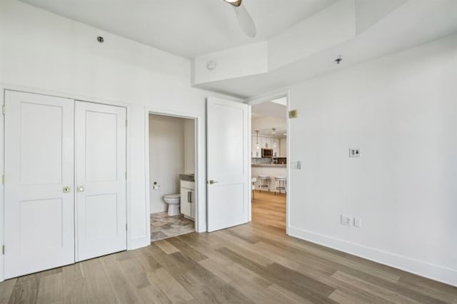 unfurnished bedroom with ensuite bath, wood-type flooring, ceiling fan, and a closet