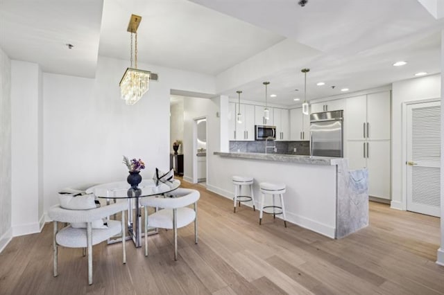 kitchen featuring light stone counters, kitchen peninsula, hanging light fixtures, stainless steel appliances, and white cabinetry