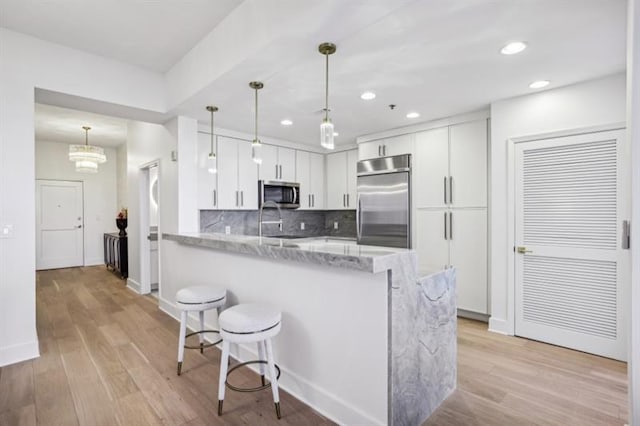 kitchen with kitchen peninsula, light stone countertops, pendant lighting, stainless steel appliances, and white cabinetry