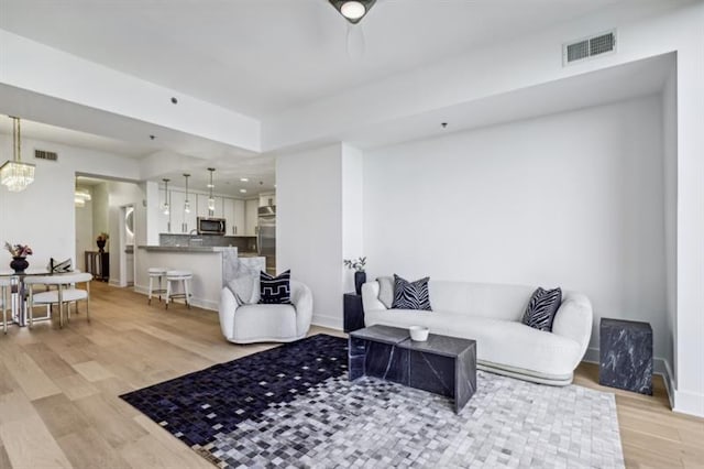 living room featuring light wood-type flooring and ceiling fan with notable chandelier