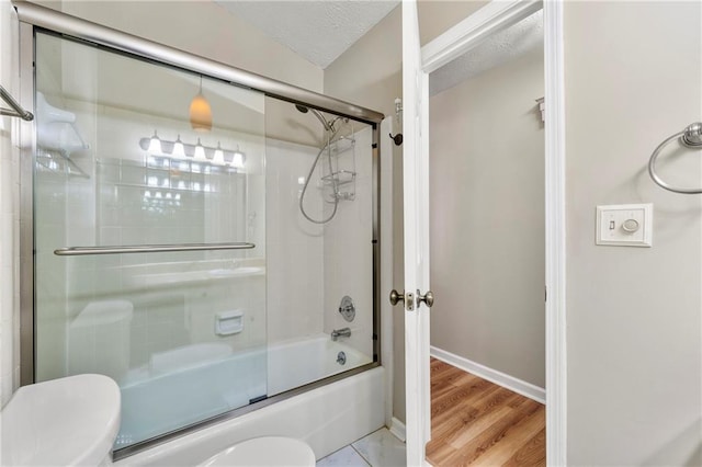 full bathroom featuring shower / bath combination with glass door, toilet, a textured ceiling, wood finished floors, and baseboards