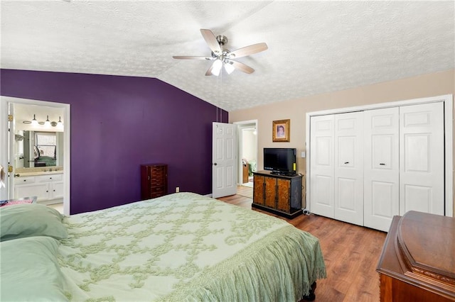 bedroom featuring lofted ceiling, ceiling fan, a textured ceiling, wood finished floors, and a closet