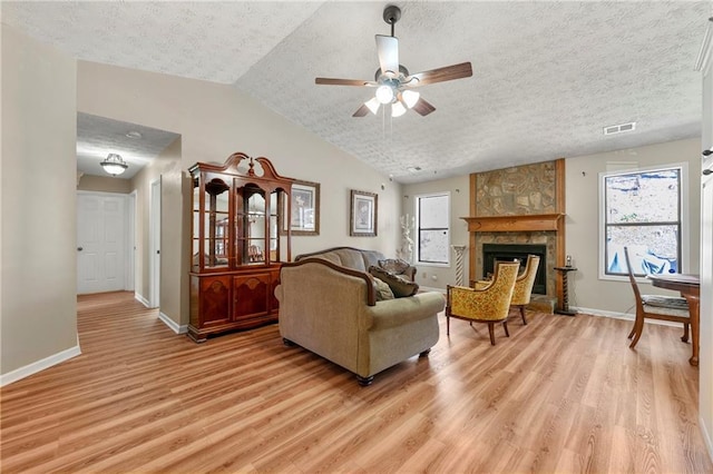 living area featuring baseboards, vaulted ceiling, a stone fireplace, and light wood finished floors