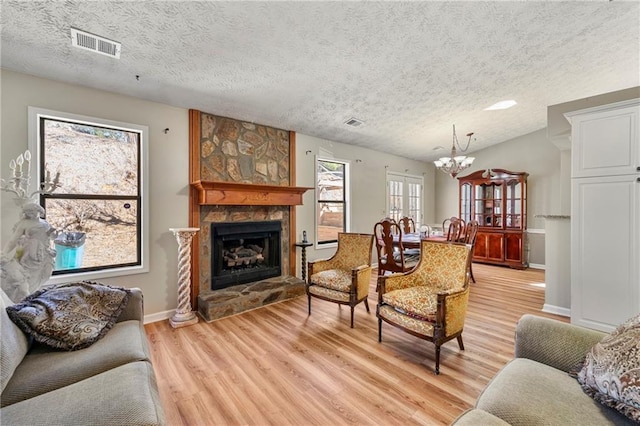 living area with visible vents, a textured ceiling, light wood-type flooring, a fireplace, and a notable chandelier