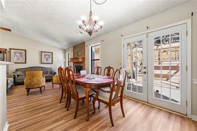 dining space with light wood finished floors, french doors, vaulted ceiling, a stone fireplace, and a notable chandelier