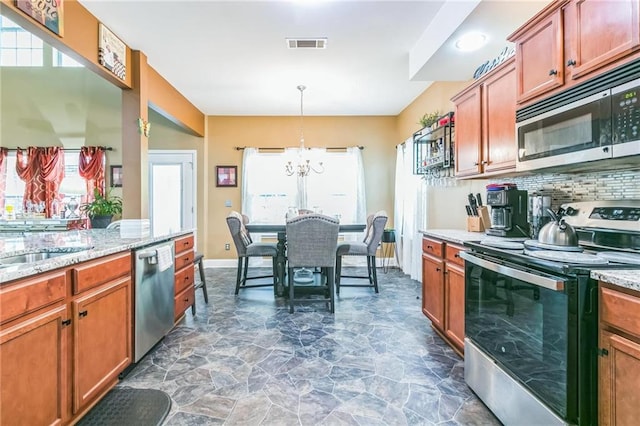 kitchen with tasteful backsplash, light stone counters, stainless steel appliances, decorative light fixtures, and a chandelier