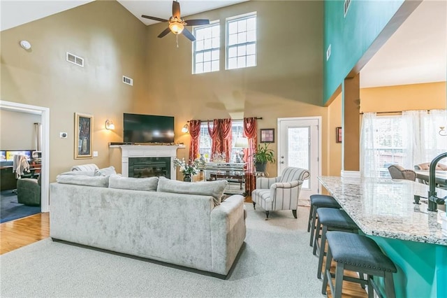 carpeted living room featuring a high ceiling, ceiling fan, and a healthy amount of sunlight