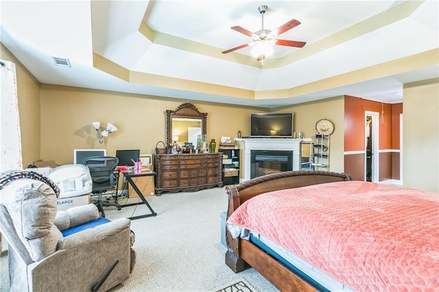 carpeted bedroom with a raised ceiling and ceiling fan