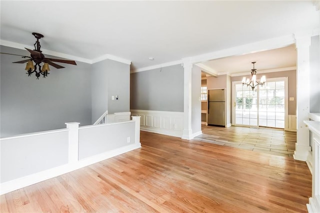 spare room featuring a chandelier, crown molding, a ceiling fan, light wood-style flooring, and a wainscoted wall