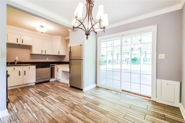 kitchen with appliances with stainless steel finishes, dark countertops, a chandelier, white cabinetry, and crown molding