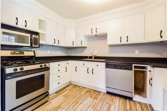 kitchen with stainless steel appliances, a sink, dark countertops, white cabinetry, and light wood finished floors