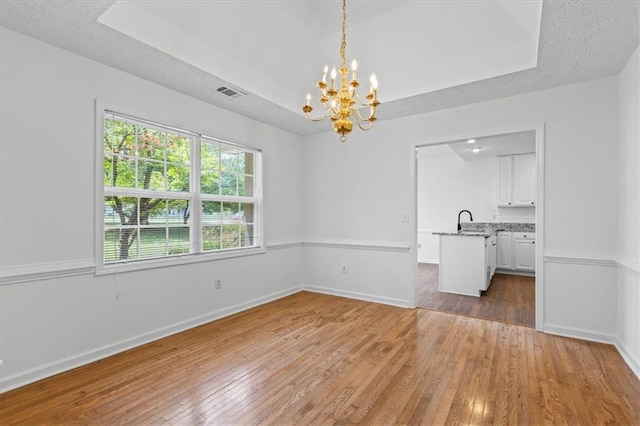 unfurnished dining area featuring wood-type flooring, a chandelier, a raised ceiling, baseboards, and a textured ceiling