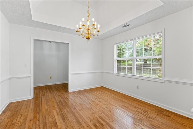 unfurnished room with a chandelier, light wood-style flooring, baseboards, a tray ceiling, and a textured ceiling