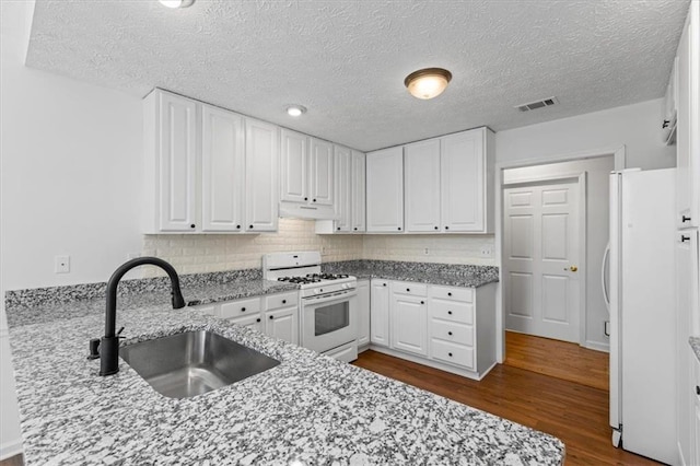 kitchen featuring white appliances, a sink, under cabinet range hood, dark wood-style floors, and white cabinetry