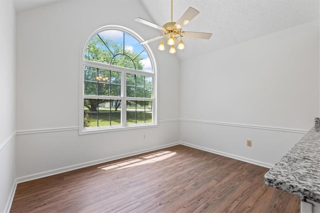 spare room featuring dark wood finished floors, lofted ceiling, baseboards, and ceiling fan