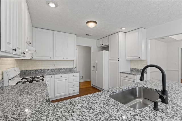 kitchen featuring white appliances, a sink, white cabinetry, light stone countertops, and a textured ceiling