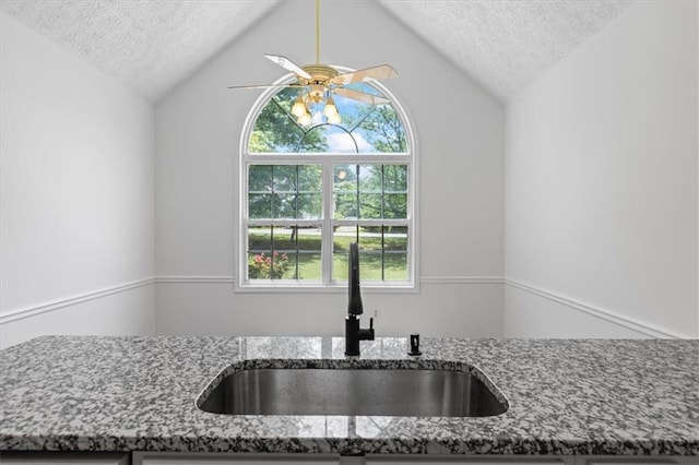 kitchen view of a sink, a textured ceiling, stone countertops, and a ceiling fan