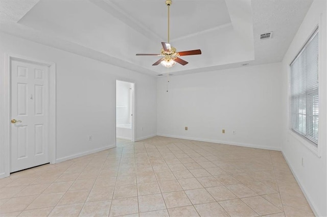 unfurnished room with a tray ceiling, a ceiling fan, baseboards, and light tile patterned flooring