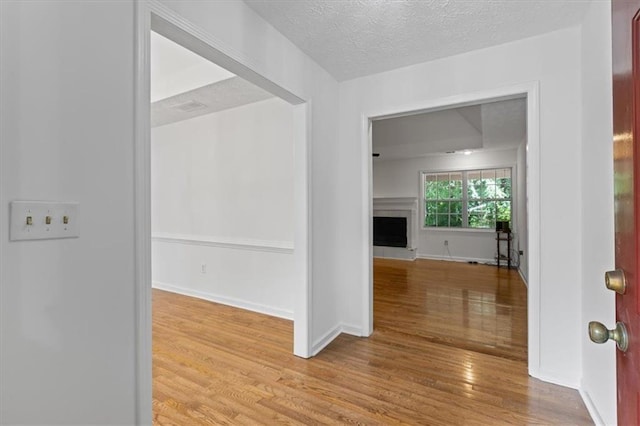 hall with wood finished floors, a textured ceiling, and baseboards