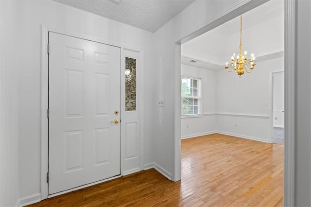 entryway with a chandelier, wood finished floors, baseboards, and a textured ceiling