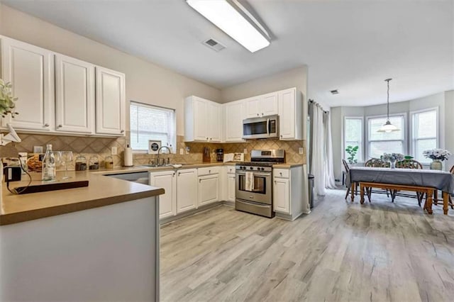 kitchen with appliances with stainless steel finishes, sink, pendant lighting, light hardwood / wood-style flooring, and white cabinetry