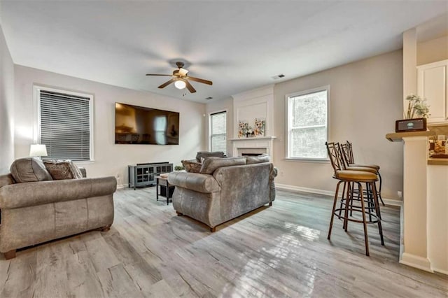 living room featuring ceiling fan, a large fireplace, and light hardwood / wood-style flooring