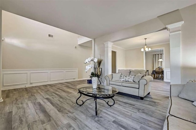 living room featuring a chandelier, wood-type flooring, decorative columns, and ornamental molding