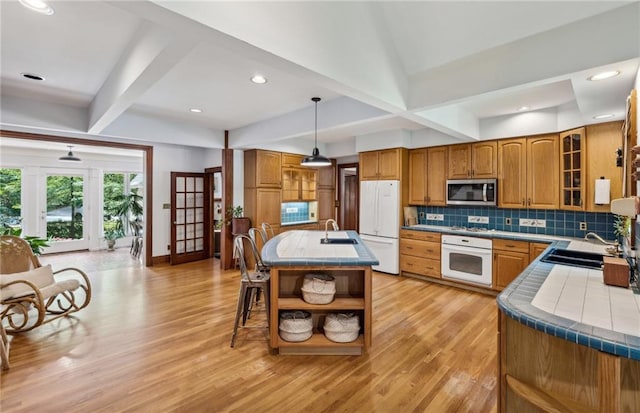 kitchen featuring white appliances, sink, light hardwood / wood-style floors, and hanging light fixtures