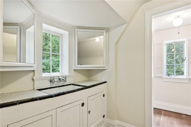 interior space featuring dark hardwood / wood-style flooring, white cabinets, tile countertops, sink, and vaulted ceiling