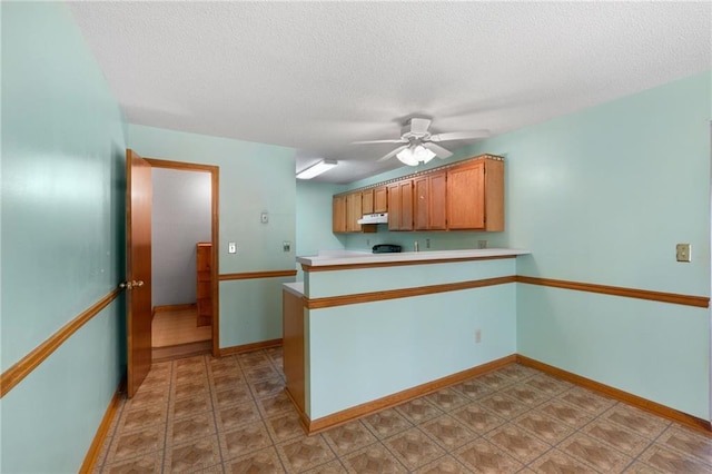kitchen with ceiling fan, light countertops, a textured ceiling, a peninsula, and under cabinet range hood