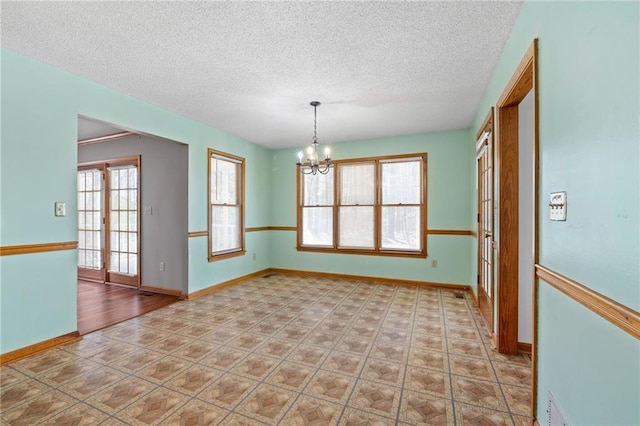 empty room featuring a textured ceiling, a chandelier, and baseboards