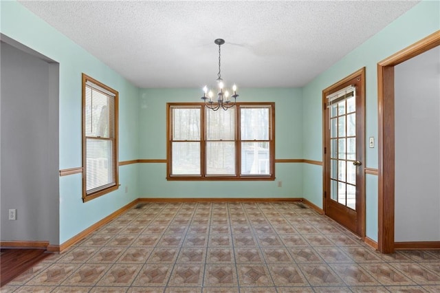 empty room featuring a textured ceiling, an inviting chandelier, and baseboards