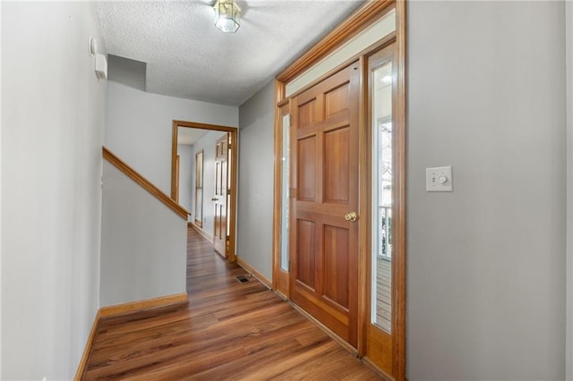entryway with baseboards, a textured ceiling, visible vents, and wood finished floors