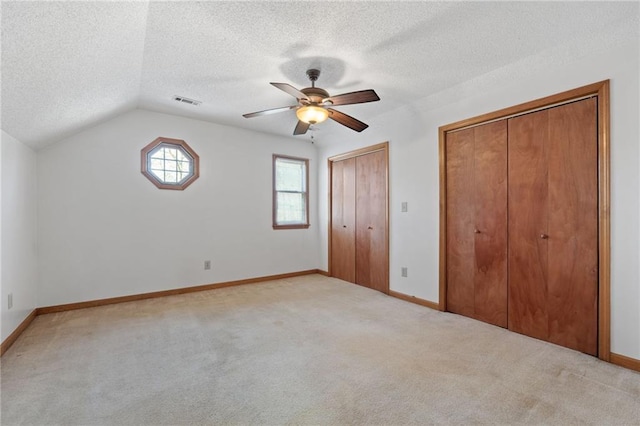 unfurnished bedroom with two closets, a textured ceiling, light colored carpet, and baseboards