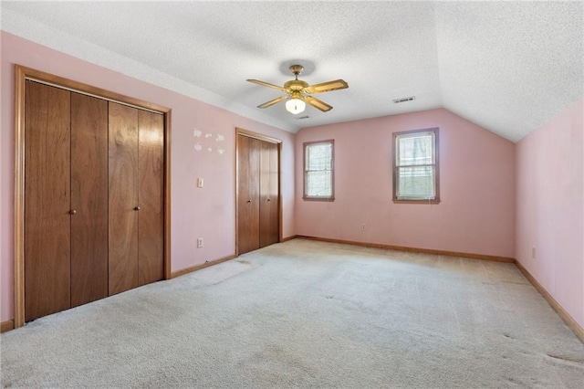 unfurnished bedroom with multiple closets, light colored carpet, a textured ceiling, and visible vents