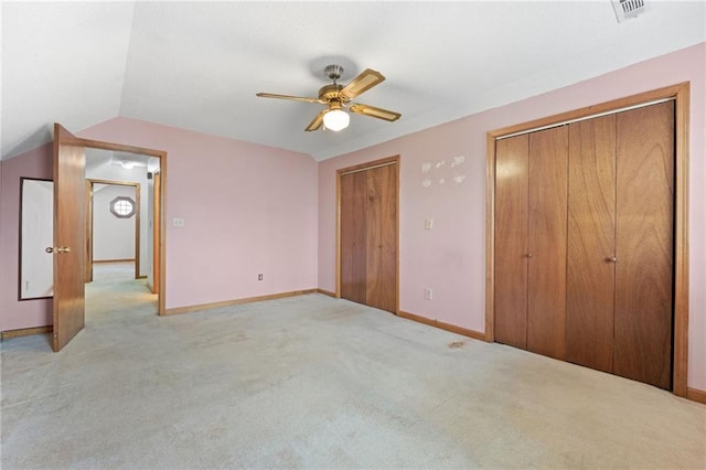 unfurnished bedroom with vaulted ceiling, baseboards, two closets, and light colored carpet