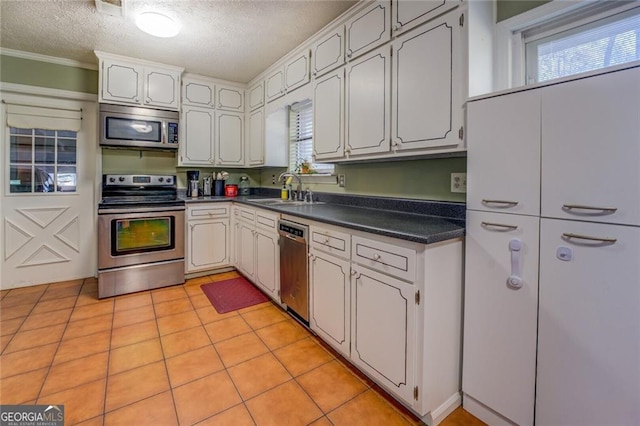 kitchen featuring sink, light tile patterned floors, stainless steel appliances, a textured ceiling, and white cabinets