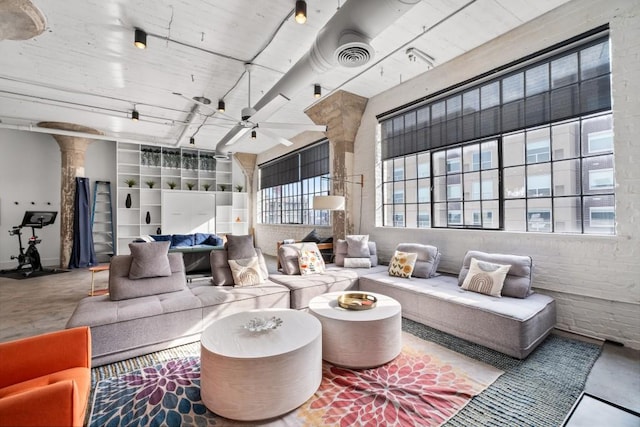 living area featuring visible vents, concrete floors, brick wall, ceiling fan, and ornate columns