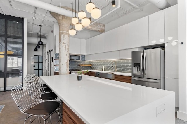 kitchen featuring ornate columns, a sink, decorative backsplash, stainless steel appliances, and white cabinets