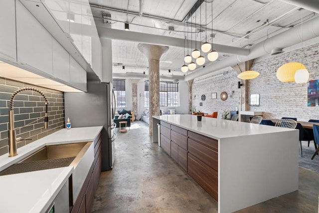 kitchen with a center island, concrete floors, light countertops, decorative columns, and a sink