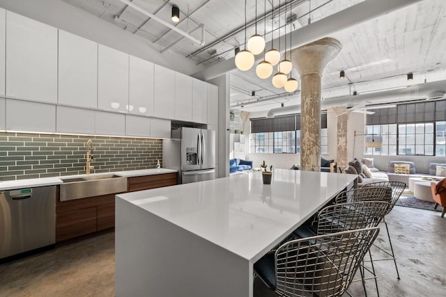 kitchen with concrete floors, light countertops, a kitchen breakfast bar, stainless steel appliances, and a sink