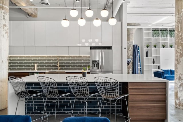 kitchen with stainless steel refrigerator with ice dispenser, a sink, a center island, white cabinetry, and light countertops