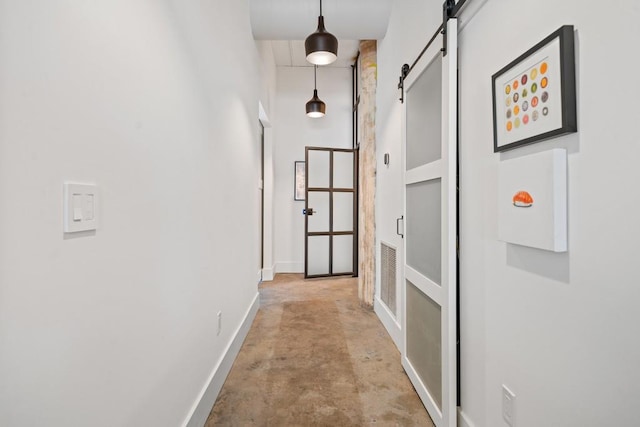 hall featuring a barn door, visible vents, baseboards, and concrete floors