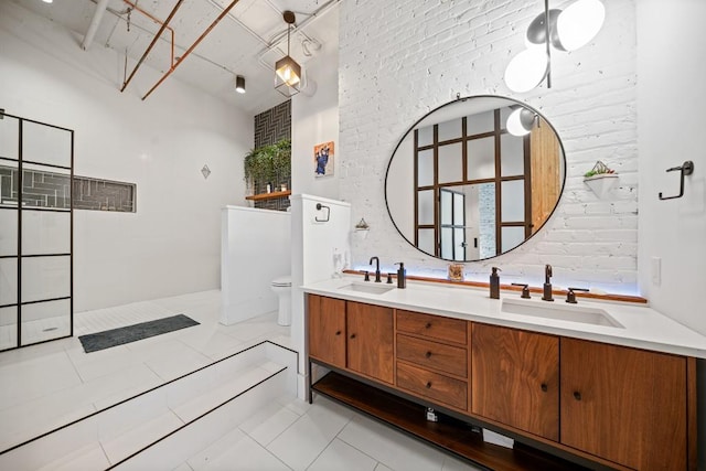 bathroom featuring double vanity, brick wall, toilet, and a sink