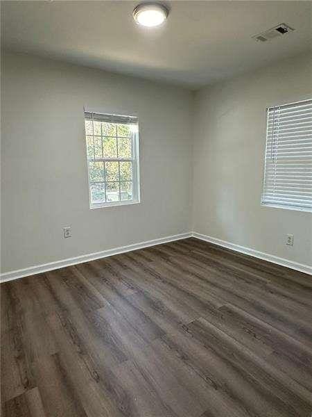 spare room featuring baseboards, dark wood-style floors, and visible vents