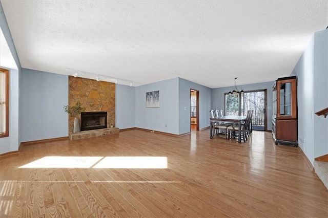 unfurnished living room featuring rail lighting, wood-type flooring, a chandelier, a textured ceiling, and a fireplace