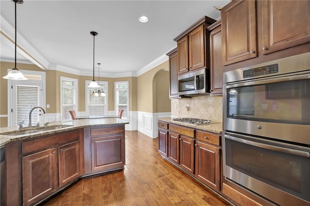 kitchen with arched walkways, a wainscoted wall, stainless steel appliances, crown molding, and a sink