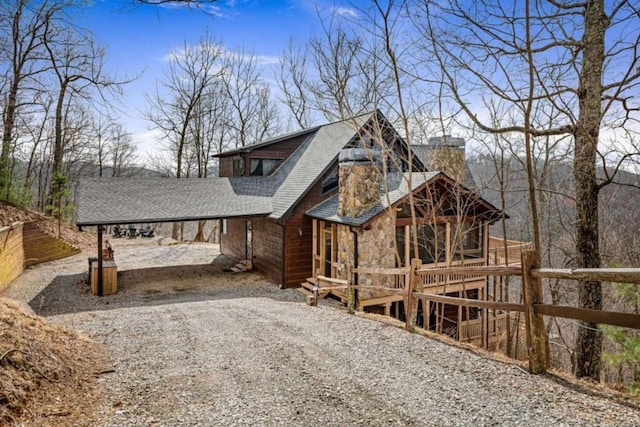 exterior space featuring fence, gravel driveway, a chimney, a carport, and stone siding