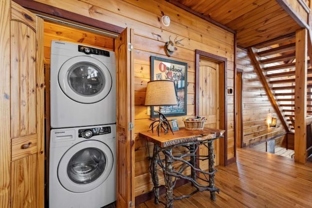 laundry area featuring stacked washer and clothes dryer, wood finished floors, wooden walls, wood ceiling, and laundry area